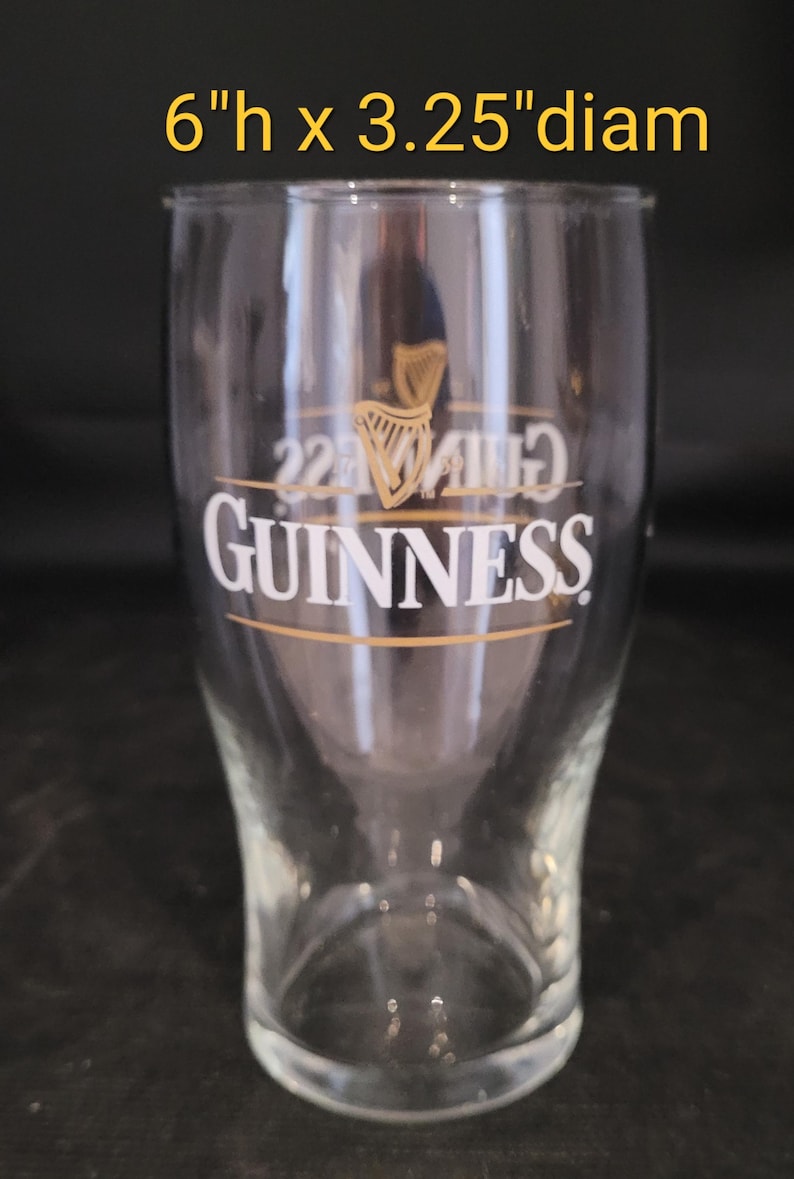 May include: Clear pint glass with the Guinness logo in gold and white. The glass is 6 inches high and 3.25 inches in diameter. The Guinness logo includes a harp symbol and the text "GUINNESS".