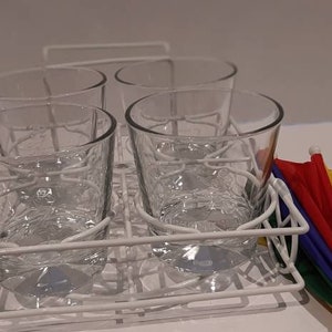 May include: Four clear glass tumblers are stacked in a white wire rack. A small rainbow-coloured umbrella is on the right side of the image.