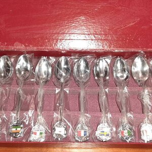 May include: A set of 12 silver teaspoons with colourful flags on the handles, displayed in a red velvet lined box.