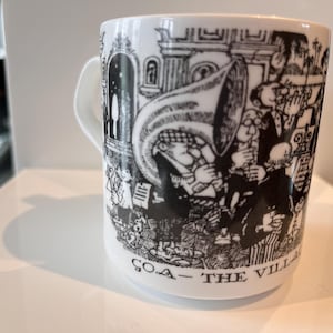May include: White ceramic mug with a black and white illustration of a band playing instruments. The mug has a handle and the words "GOA - THE VILLAGE" are printed on the bottom.