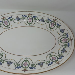 May include: Oval serving platter with a white background and a gold rim. The platter is decorated with a repeating pattern of pink, green, and blue floral and scroll designs. A gold line borders the inner oval.
