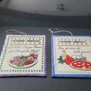 May include: Two Italian proverb ceramic tiles. One tile has an illustration of a plate of food and the text "La Vita è Troppo Breve per Mangiare Male!" The other tile has a pizza illustration and the text "Non si vive di solo pane!"