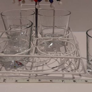 May include: A white metal rack with four clear glass cups. The rack is designed to hold the cups upside down for drying.