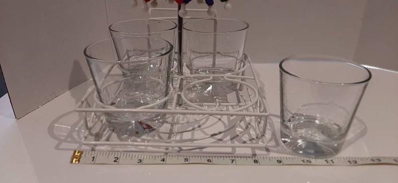 May include: A white metal rack with four clear glass cups. The rack is designed to hold the cups upside down for drying.