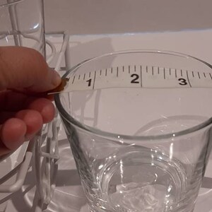 May include: A clear glass measuring jug with a white tape measure around the top. The tape measure reads "1, 2, 3, 4".