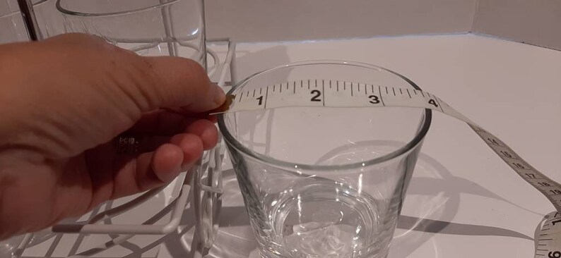 May include: A clear glass measuring jug with a white tape measure around the top. The tape measure reads "1, 2, 3, 4".
