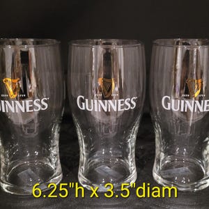May include: Three clear Guinness pint glasses. Each glass has the Guinness logo in white and gold. The glasses are 6.25 inches high and 3.5 inches in diameter. The glasses are empty and ready to be filled.