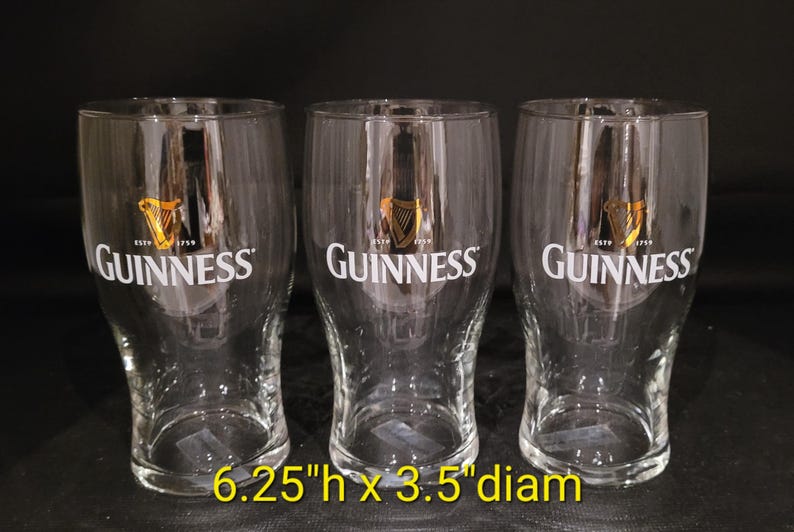 May include: Three clear Guinness pint glasses. Each glass has the Guinness logo in white and gold. The glasses are 6.25 inches high and 3.5 inches in diameter. The glasses are empty and ready to be filled.
