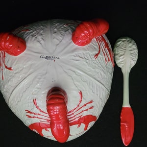 Puede incluir: Tazón de servir de cerámica blanca con diseño de langosta roja y una cuchara de servir a juego roja y blanca. El tazón tiene el texto "Carlton Ware" en la parte inferior.