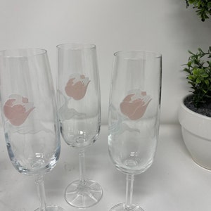 May include: Three clear glass champagne flutes with a pink floral design etched on the side.