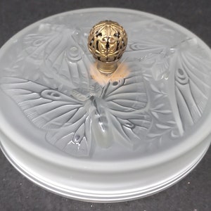 May include: A frosted glass lid with a decorative butterfly design and a gold metal knob. The lid is round and has a raised edge.
