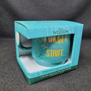 May include: A turquoise blue ceramic mug with a green and white design. The mug has the text "Forget about your worries and your strife" on it. The mug is in a box with the text "Disney Wisdom" on it.