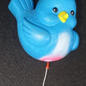 May include: A blue plastic bird with a yellow beak and white accents. The bird is attached to a string with a yellow ring at the end.