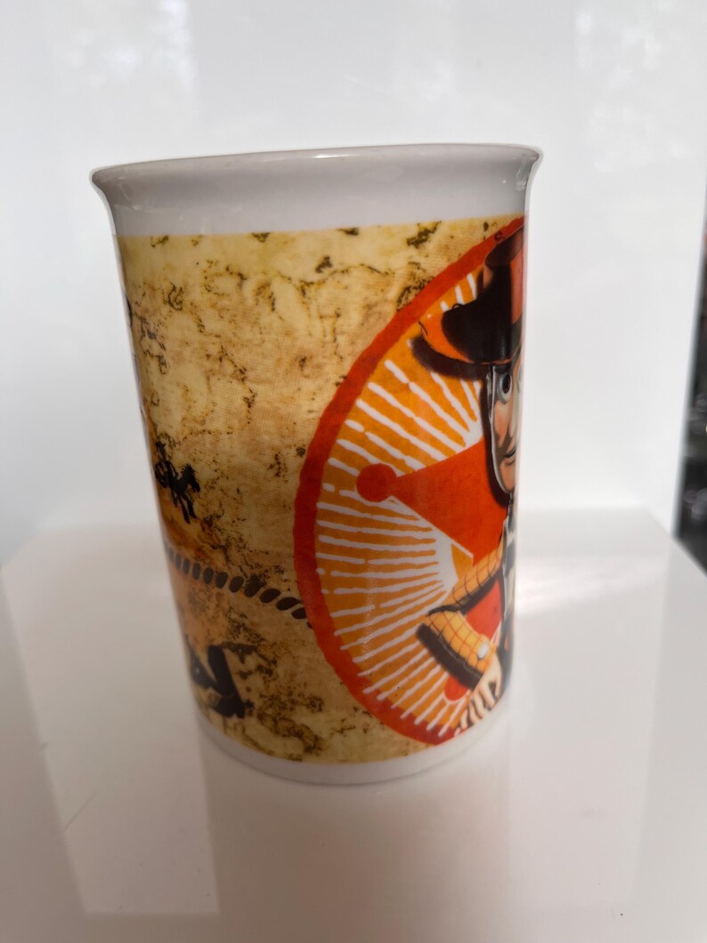 K&ouml;nnte beinhalten: Wei&szlig;er Keramikbecher mit einem Cartoon-Cowboy-Design. Der Becher hat einen beigefarbenen, strukturierten Hintergrund und ein orange-wei&szlig;es kreisf&ouml;rmiges Design. Der Cowboy tr&auml;gt einen Hut und eine Weste. Geeignet f&uuml;r Hei&szlig;getr&auml;nke.