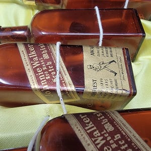 May include: A collection of miniature glass bottles with labels for Johnnie Walker Scotch Whisky. The bottles are tied together with string and feature a gold label with the text "Johnnie Walker" and "Scotch Whisky".