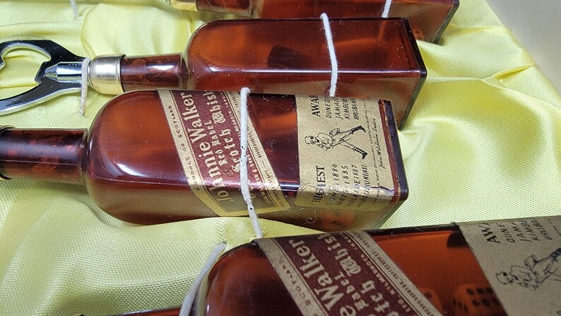 May include: A collection of miniature glass bottles with labels for Johnnie Walker Scotch Whisky. The bottles are tied together with string and feature a gold label with the text "Johnnie Walker" and "Scotch Whisky".
