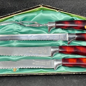 May include: A vintage carving set with four knives and a fork, presented in a decorative box. The knives and fork have stainless steel blades and handles with a tortoiseshell pattern and yellow accents. The box is lined with green satin.