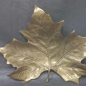 Op de afbeelding: Een blad van goudkleurig metaal met gedetailleerde nerven en een textuur.