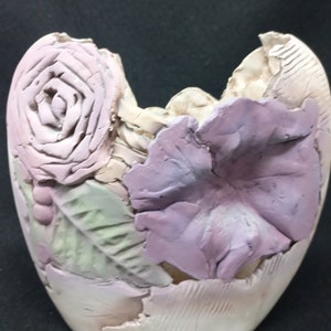 May include: A ceramic vase with a textured surface, decorated with sculpted flowers in shades of pink, purple, and green.