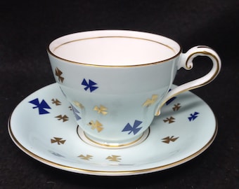 May include: A light blue teacup and saucer set with a gold trim and a pattern of blue and gold stylized crosses.