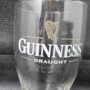 May include: A clear Guinness pint glass with the Guinness logo, a harp, and the word "Draught" printed on the front. The glass has the numbers "17" and "59" printed above the logo.