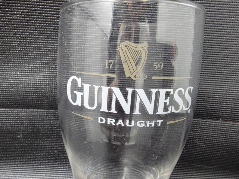 May include: A clear Guinness pint glass with the Guinness logo, a harp, and the word "Draught" printed on the front. The glass has the numbers "17" and "59" printed above the logo.