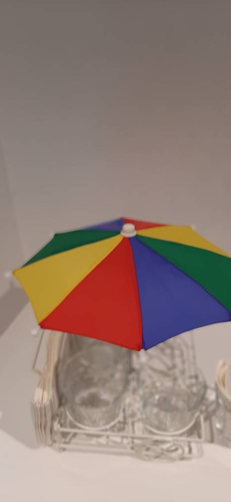 May include: A colourful, multi-coloured, small umbrella with red, yellow, blue, and green panels. The umbrella is sitting on top of a white wire rack.