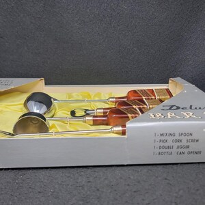 May include: A silver bar set in a box with a yellow lining. The set includes a mixing spoon, a cork screw, a double jigger, and a bottle can opener. The box is labeled "Deluxe Bar Set".