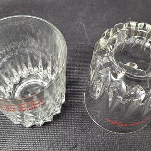 May include: Two clear, cut-glass tumblers with a diamond pattern and a scalloped rim. The text "Johnnie Walker" is printed in red near the base of each glass. The glasses are likely for serving whiskey or other spirits.