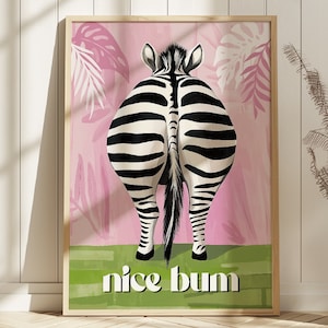 K&ouml;nnte beinhalten: Gerahmter Kunstdruck mit dem Hinterteil eines Zebras mit schwarz-wei&szlig;en Streifen, vor einem rosa Hintergrund mit wei&szlig;en und rosa Blattmustern. Der Schriftzug "nice bum" ist unten auf einem gr&uuml;nen Streifen wei&szlig; gedruckt.