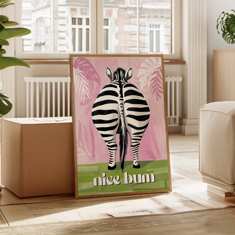 K&ouml;nnte beinhalten: Ein gerahmter Kunstdruck mit dem Hinterteil eines Zebras, mit schwarz-wei&szlig;en Streifen vor einem rosa Hintergrund mit gr&uuml;nem Gras und dem Schriftzug "nice bum". Das Kunstwerk hat einen braunen Rahmen.