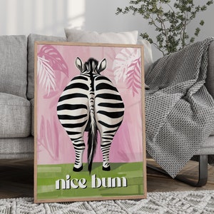 K&ouml;nnte beinhalten: Gerahmter Kunstdruck mit dem Hinterteil eines Zebras mit schwarz-wei&szlig;en Streifen vor einem rosa Hintergrund mit tropischen Bl&auml;ttern. Der Schriftzug "nice bum" steht in Wei&szlig; auf einem gr&uuml;nen Streifen.