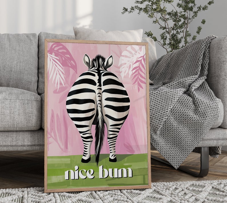 K&ouml;nnte beinhalten: Gerahmter Kunstdruck mit dem Hinterteil eines Zebras mit schwarz-wei&szlig;en Streifen vor einem rosa Hintergrund mit tropischen Bl&auml;ttern. Der Schriftzug "nice bum" steht in Wei&szlig; auf einem gr&uuml;nen Streifen.