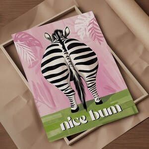 K&ouml;nnte beinhalten: Gerahmter Kunstdruck mit dem Hinterteil eines Zebras mit schwarz-wei&szlig;en Streifen, vor einem rosa Hintergrund mit Bl&auml;ttern. Der Schriftzug "nice bum" ist wei&szlig; auf einem gr&uuml;nen Streifen unten gedruckt.