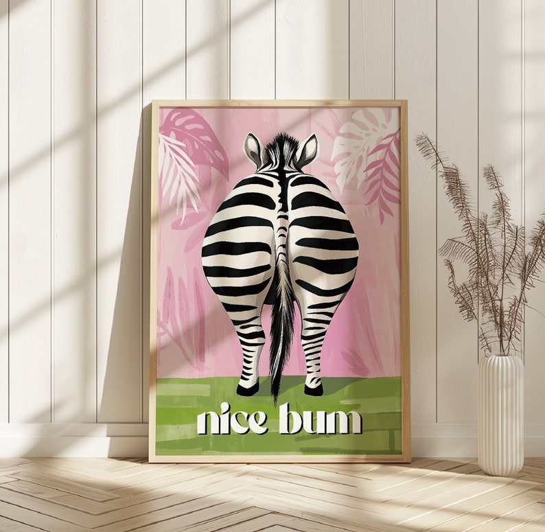 K&ouml;nnte beinhalten: Gerahmter Kunstdruck mit dem Hinterteil eines Zebras mit schwarz-wei&szlig;en Streifen, vor einem rosa Hintergrund mit wei&szlig;en und rosa Blattmustern. Der Schriftzug "nice bum" ist unten auf einem gr&uuml;nen Streifen wei&szlig; gedruckt.