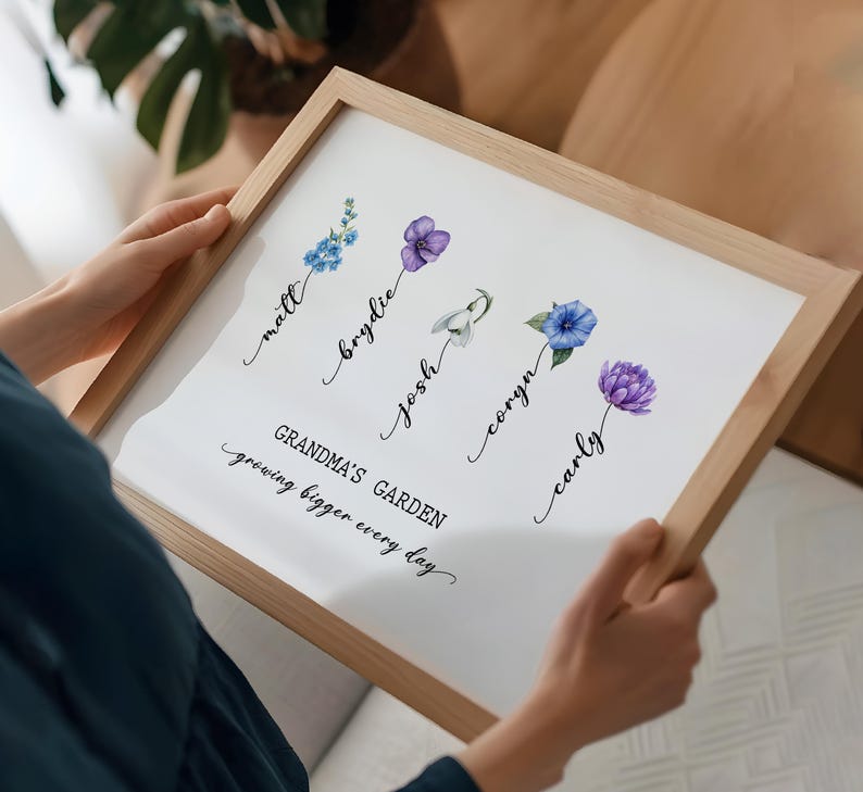 May include: A white framed print with a floral design and the text "Grandma's Garden growing bigger every day". The flowers are purple, blue, and white and are arranged in a vertical line. Each flower is labeled with a name: Matt, Brydie, Josh, Coryn, and Carly.