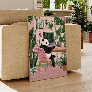 Op de afbeelding: Een zwart-witte pandabeer zit aan een bureau voor een computerscherm met groene planten en bloemen op de achtergrond. De panda draagt een roze stoel en heeft zijn poten op het toetsenbord. Het computerscherm toont code.