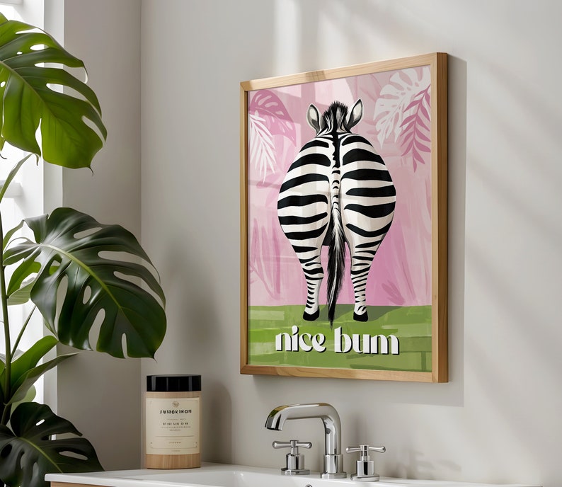 K&ouml;nnte beinhalten: Gerahmter Kunstdruck mit dem Hinterteil eines Zebras, mit schwarz-wei&szlig;en Streifen, vor einem rosa-gr&uuml;nen Hintergrund. Der Text "nice bum" ist in Wei&szlig; dargestellt. Das Kunstwerk befindet sich in einem hellen Holzrahmen.