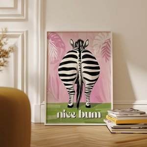 K&ouml;nnte beinhalten: Ein gerahmter Kunstdruck mit dem Hinterteil eines Zebras mit schwarz-wei&szlig;en Streifen, vor einem rosa Hintergrund mit Blattmustern. Der Satz "nice bum" steht in Wei&szlig; unten auf einem gr&uuml;nen Streifen.