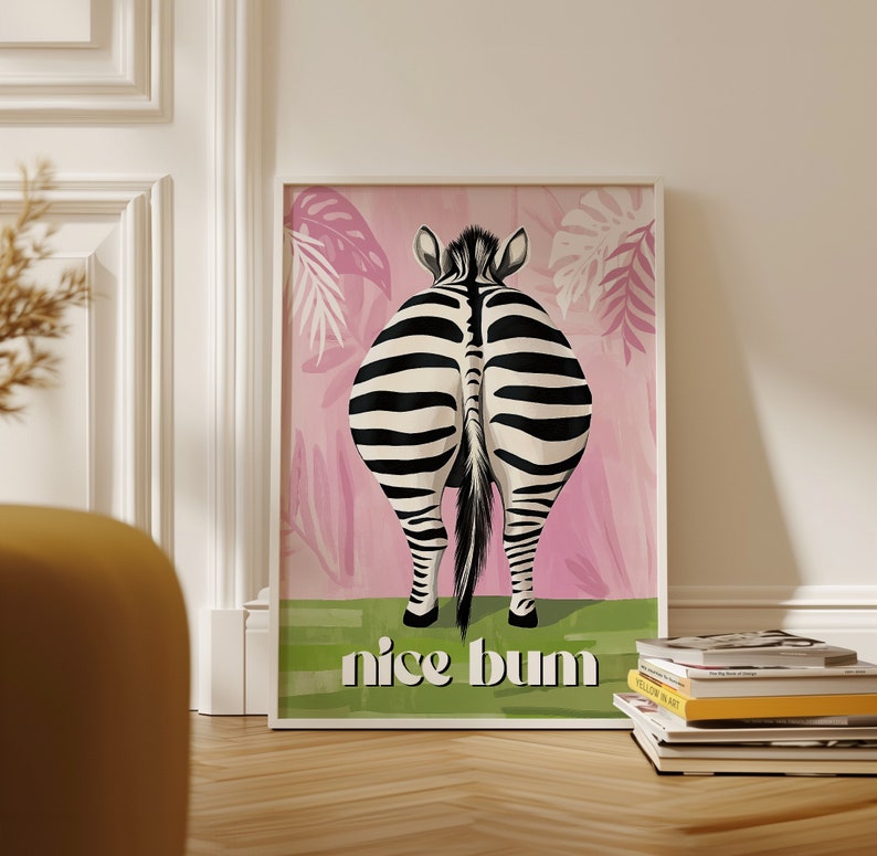 K&ouml;nnte beinhalten: Ein gerahmter Kunstdruck mit dem Hinterteil eines Zebras mit schwarz-wei&szlig;en Streifen, vor einem rosa Hintergrund mit Blattmustern. Der Satz "nice bum" steht in Wei&szlig; unten auf einem gr&uuml;nen Streifen.