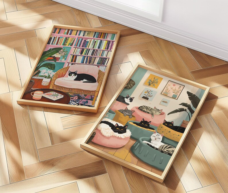 May include: Two framed art prints featuring cat illustrations. One print depicts a cat lounging in a chair in a room with a bookshelf. The other shows multiple cats in beds. Both prints have wooden frames.