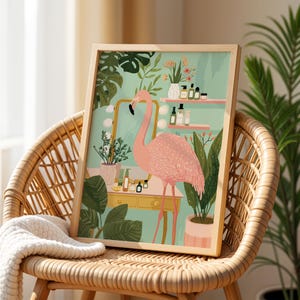 May include: Framed art print depicting a pink flamingo in a bathroom scene. The illustration shows a vanity with a mirror, plants, and beauty products. The artwork is displayed on a wicker chair with a cream blanket.