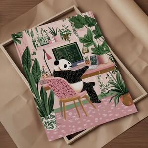 Op de afbeelding: Een zwart-witte pandabeer zit aan een roze bureau met een computerscherm waarop code wordt weergegeven. De panda zit op een roze stoel met witte stippen. Het bureau is omringd door weelderige groene planten in een roze kamer.