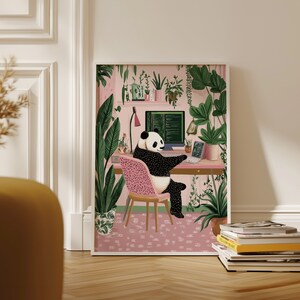 Op de afbeelding: Een zwart-witte pandabeer zit aan een bureau voor een computerscherm met code die erop wordt weergegeven. De panda zit op een roze stoel en er zijn planten op de achtergrond. De kamer is ingericht in een roze en groene kleurstelling.