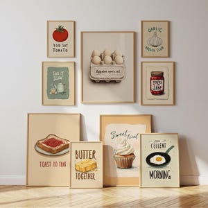 May include: A gallery wall set of eight framed art prints featuring food illustrations with text. Prints include a tomato, a carton of eggs labeled Eggstra special, a garlic bulb, a jar of jam, toast, butter, a cupcake, and a fried egg in a pan.