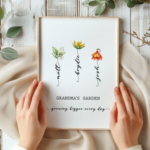 May include: A framed print with a white background and three watercolor flowers. The flowers are labeled "Josh", "Brydie", and "Matt". The text below the flowers reads "Grandma's Garden growing bigger every day".