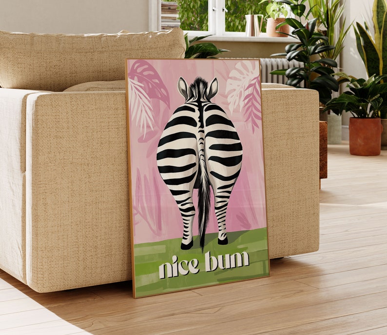 K&ouml;nnte beinhalten: Ein gerahmter Kunstdruck mit dem Hinterteil eines Zebras mit schwarz-wei&szlig;en Streifen, vor einem rosa Hintergrund mit tropischen Bl&auml;ttern. Der Schriftzug "nice bum" steht in Gr&uuml;n am unteren Rand.