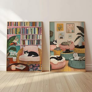May include: Two framed art prints featuring cats. One shows a black and white cat on a pink chair in front of a bookshelf. The other depicts multiple cats lounging on cushions. Both have gold frames.