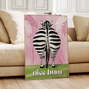 K&ouml;nnte beinhalten: Gerahmter Kunstdruck mit dem Hinterteil eines Zebras mit schwarz-wei&szlig;en Streifen, vor einem rosa Hintergrund mit tropischen Bl&auml;ttern. Der Schriftzug "nice bum" steht in wei&szlig;en Buchstaben auf gr&uuml;nem Grund.