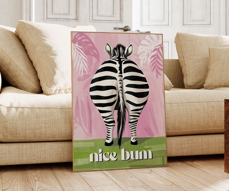 K&ouml;nnte beinhalten: Gerahmter Kunstdruck mit dem Hinterteil eines Zebras mit schwarz-wei&szlig;en Streifen, vor einem rosa Hintergrund mit tropischen Bl&auml;ttern. Der Schriftzug "nice bum" steht in wei&szlig;en Buchstaben auf gr&uuml;nem Grund.